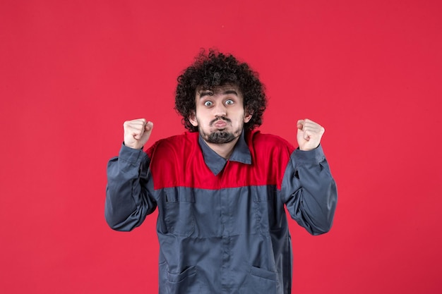 Vista frontal trabajador de sexo masculino en uniforme sobre fondo rojo uniforme herramienta mecánica foto trabajador de la casa trabajo de instrumentos de color