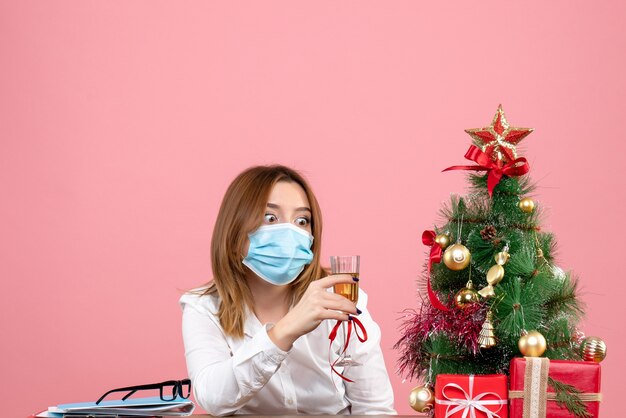 Vista frontal de la trabajadora en máscara estéril celebrando la Navidad con champán en rosa