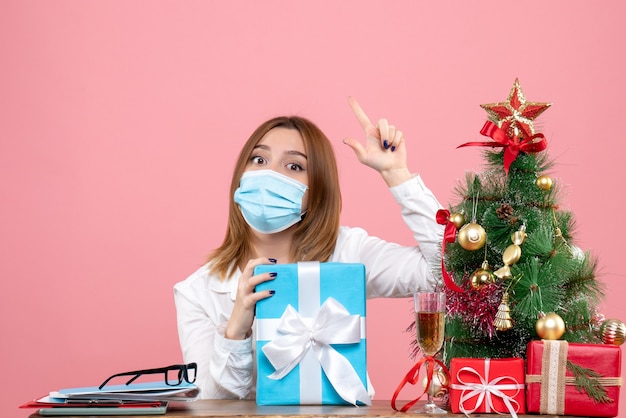 Vista frontal de la trabajadora en máscara estéril con regalos en rosa