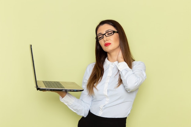 Vista frontal de la trabajadora de oficina en camisa blanca y falda negra sosteniendo y usando la computadora portátil en la pared verde