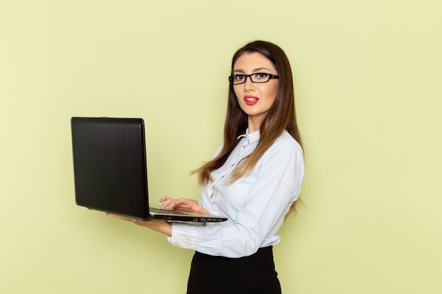 Vista frontal de la trabajadora de oficina en camisa blanca y falda negra usando su computadora portátil en el escritorio verde claro trabajador de oficina trabajo de trabajo ocupado