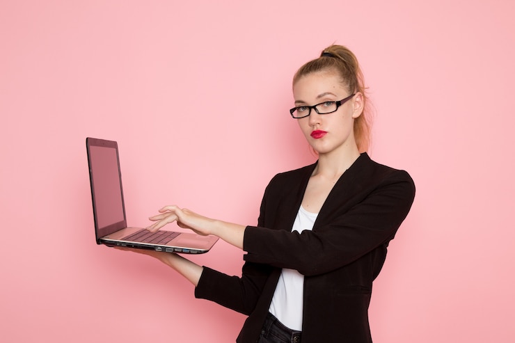 Foto gratuito vista frontal de la trabajadora de oficina en chaqueta negra estricta usando su computadora portátil en la pared rosa claro