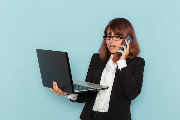 Vista frontal de la trabajadora de oficina hablando por teléfono y sosteniendo la computadora portátil en la superficie azul