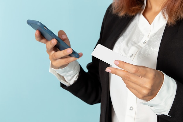 Vista frontal de la trabajadora de oficina usando su teléfono y sosteniendo la tarjeta en la superficie azul