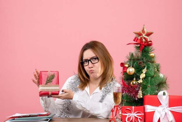 Vista frontal de la trabajadora sentada alrededor de regalos de Navidad y árbol en rosa