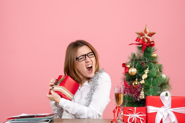 Vista frontal de la trabajadora sentada alrededor de regalos de Navidad y árbol en rosa