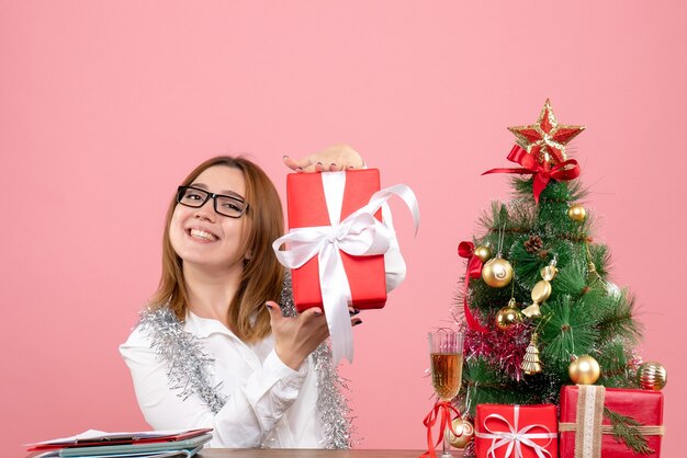 Vista frontal de la trabajadora sentada alrededor de regalos de Navidad y árbol en rosa