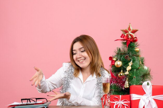 Vista frontal de la trabajadora sentada alrededor de regalos de Navidad en rosa