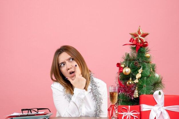 Vista frontal de la trabajadora sentada alrededor de regalos de Navidad en rosa