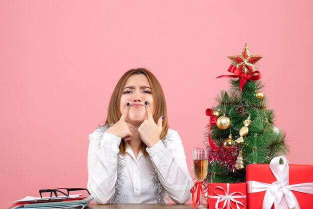 Vista frontal de la trabajadora sentada alrededor de regalos de Navidad en rosa