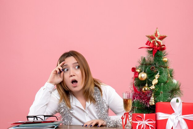 Vista frontal de la trabajadora sentada alrededor de regalos de Navidad en rosa