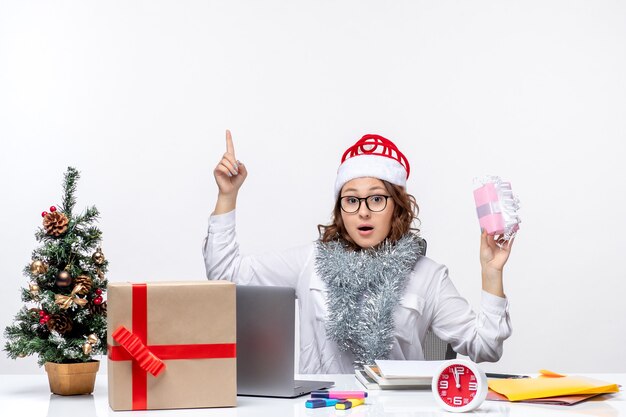 Vista frontal trabajadora sentada antes de su lugar de trabajo sosteniendo poca mujer presente trabajo trabajo de navidad oficina de negocios