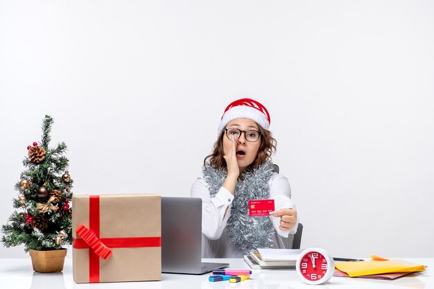 Vista frontal trabajadora sentada antes de su lugar de trabajo con tarjeta bancaria roja mujer trabajo trabajo de oficina de navidad