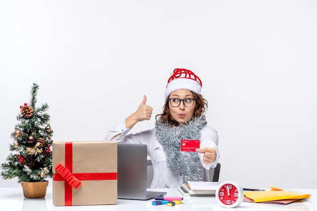 Vista frontal trabajadora sentada antes de su lugar de trabajo con tarjeta bancaria roja trabajo trabajo navidad