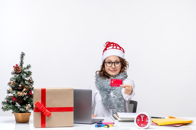 Vista frontal trabajadora sentada antes de su lugar de trabajo con tarjeta bancaria roja trabajo trabajo oficina de navidad