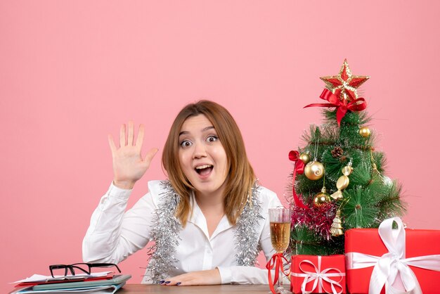 Vista frontal de la trabajadora sentada detrás de su mesa con regalos de Navidad en rosa