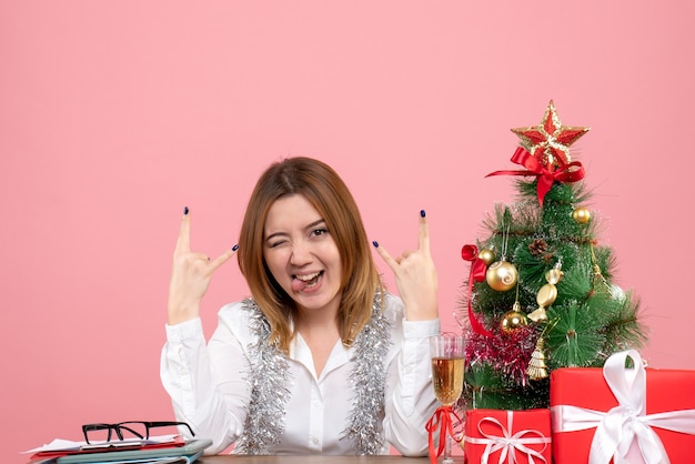 Vista frontal de la trabajadora sentada detrás de su mesa con regalos posando en rosa