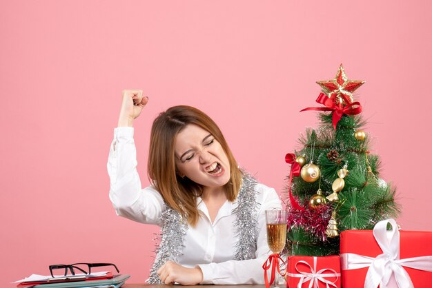 Vista frontal de la trabajadora sentada detrás de su mesa con regalos regocijándose en rosa