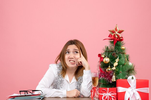 Vista frontal de la trabajadora sentada detrás de su mesa con regalos en rosa