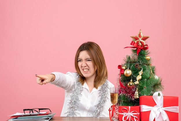 Vista frontal de la trabajadora sentada detrás de su mesa con regalos en rosa