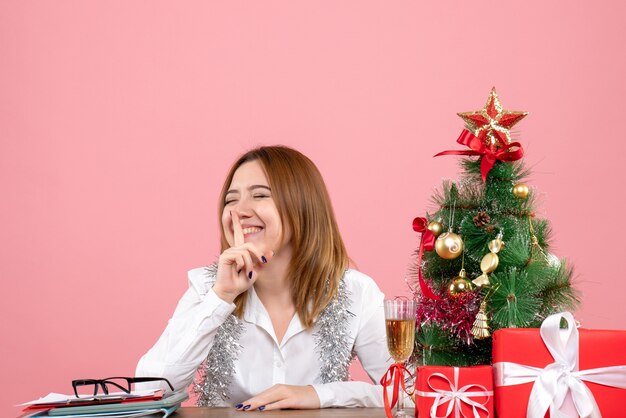 Vista frontal de la trabajadora sentada detrás de su mesa con regalos en rosa