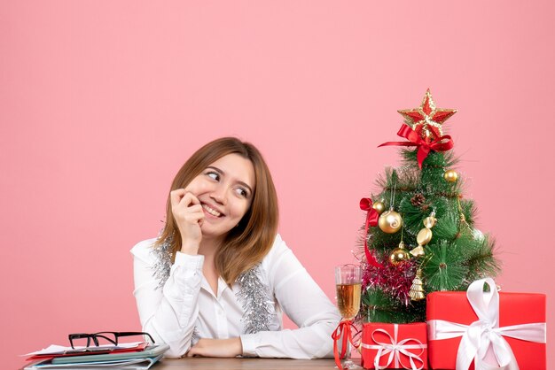 Vista frontal de la trabajadora sentada detrás de su mesa con regalos en rosa