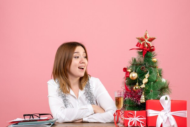 Vista frontal de la trabajadora sentada con regalos en la mesa en rosa