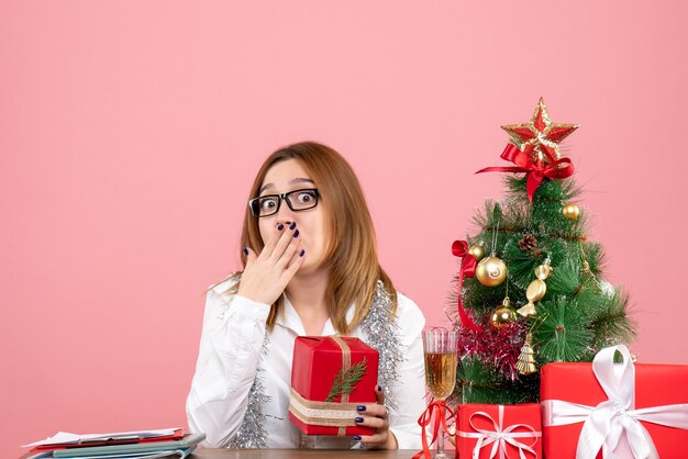 Vista frontal de la trabajadora sentada con regalos de Navidad en rosa