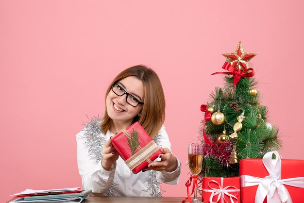 Vista frontal de la trabajadora sentada con regalos de Navidad en rosa