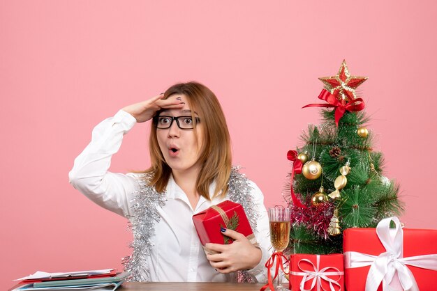 Vista frontal de la trabajadora sentada con regalos de Navidad en rosa