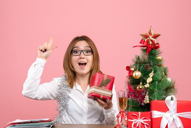 Vista frontal de la trabajadora sentada con regalos de Navidad en rosa