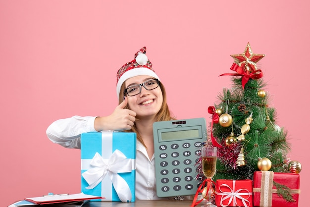 Vista frontal de la trabajadora sosteniendo la calculadora alrededor de regalos en rosa