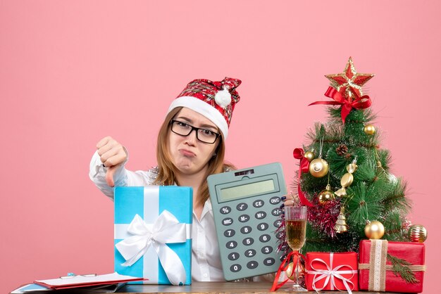 Vista frontal de la trabajadora sosteniendo la calculadora alrededor de regalos en rosa