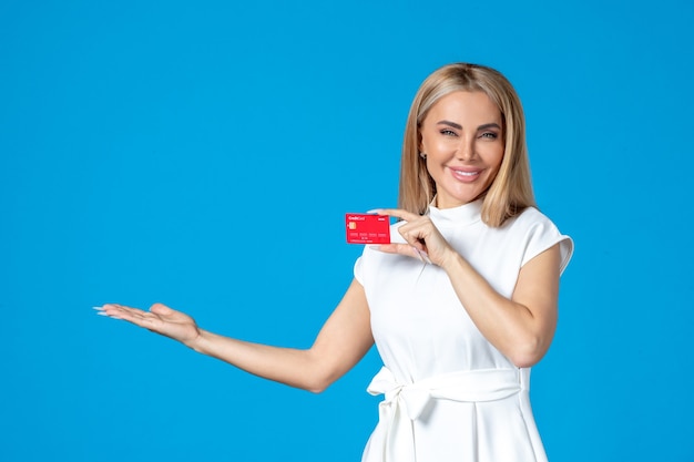 Vista frontal de la trabajadora con tarjeta bancaria roja en la pared azul