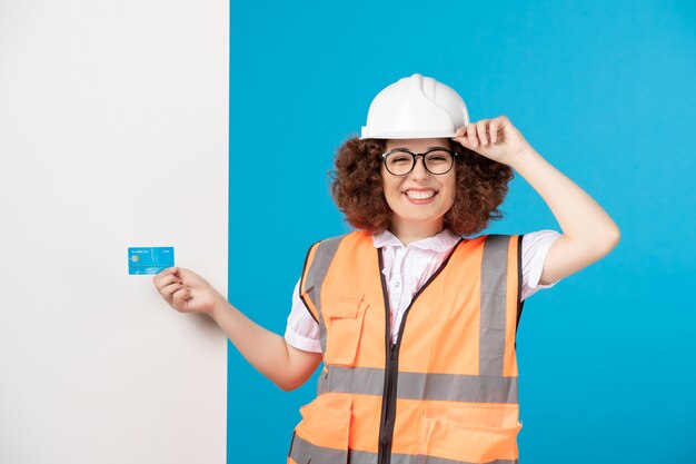 Vista frontal de la trabajadora en uniforme con tarjeta de crédito azul en la pared azul