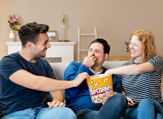 Vista frontal de tres amigos comiendo palomitas de maíz en casa