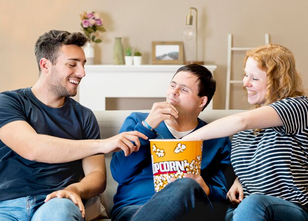 Vista frontal de tres amigos comiendo palomitas de maíz en el sofá