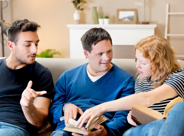 Vista frontal de tres amigos leyendo en el sofá en casa