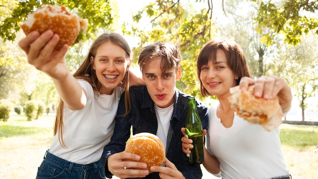 Vista frontal de tres amigos en el parque con hamburguesas y cerveza