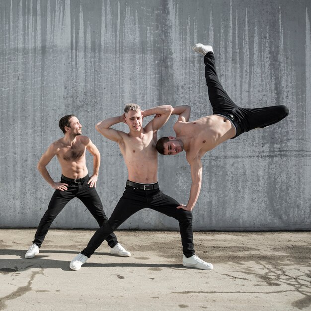 Vista frontal de tres artistas de hip hop sin camisa posando afuera