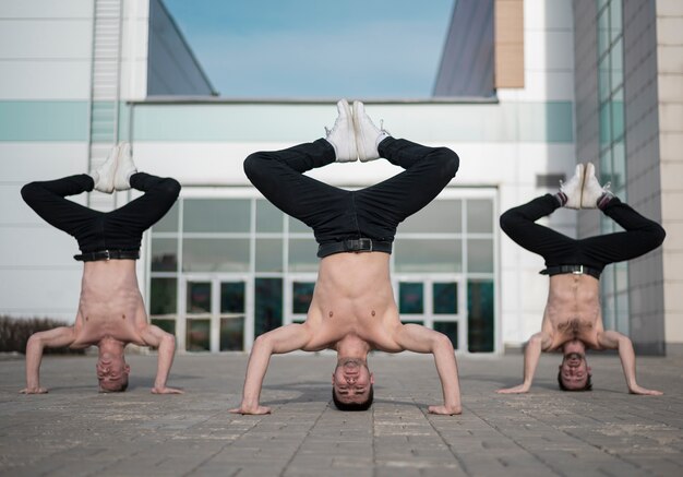 Vista frontal de tres bailarines de hip hop sin camisa de pie sobre sus cabezas