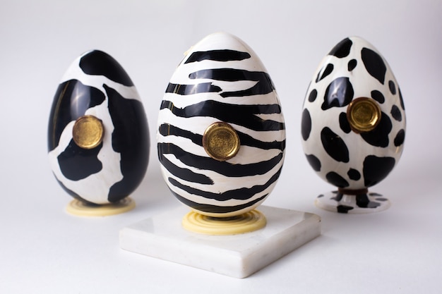 Vista frontal tres huevos de chocolate en blanco y negro en el color de una vaca cebra y dolmatins en el stand