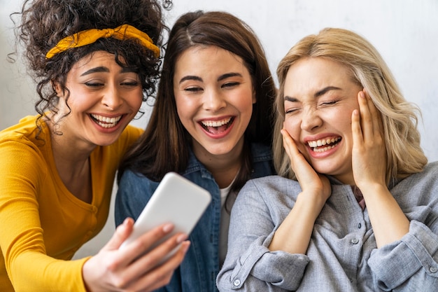 Vista frontal de tres mujeres felices sonriendo y tomando un selfie