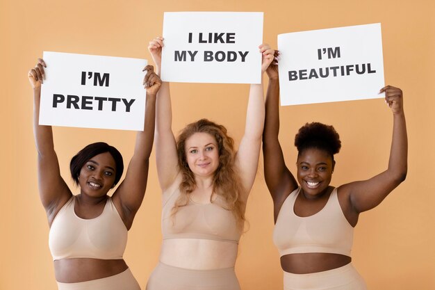 Vista frontal de tres mujeres sosteniendo pancartas con declaraciones de positividad corporal