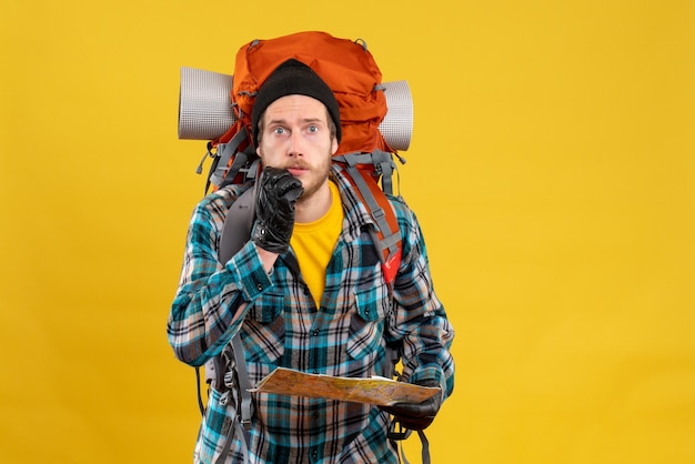 Vista frontal del turista joven desconcertado con guantes de cuero y mochila con mapa