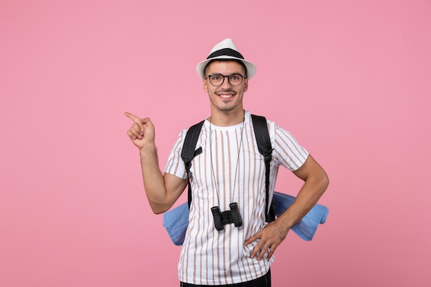 Vista frontal turista masculino sonriendo con su mochila en la pared rosa emoción color turístico