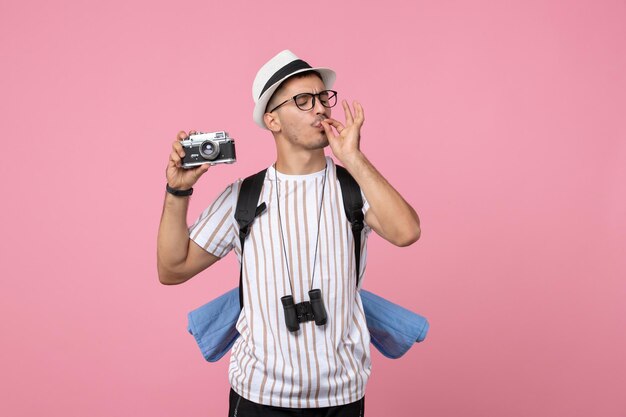 Vista frontal turista masculino sosteniendo la cámara en la pared rosa color de emociones turísticas