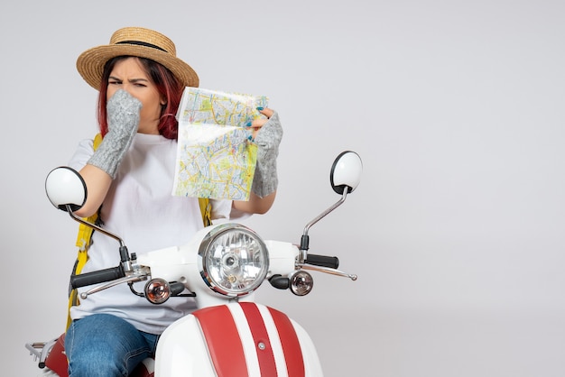 Vista frontal turista sentada en motocicleta sosteniendo mapa pared blanca