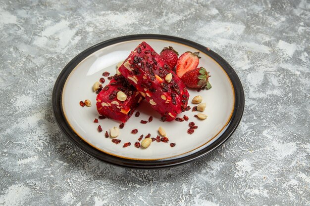 Vista frontal de turrón rojo en rodajas con nueces y fresas rojas frescas sobre superficie blanca postre dulce turrón pastel de nueces galleta galleta