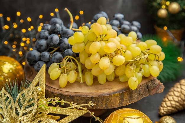 Vista frontal de uvas frescas alrededor de juguetes de navidad sobre fondo oscuro color vino de frutas navidad